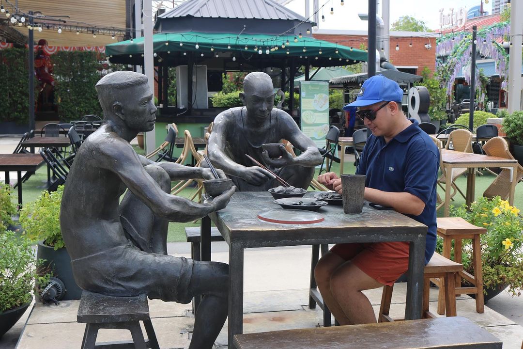 A man posing with sculptures eating food at Asiatique.