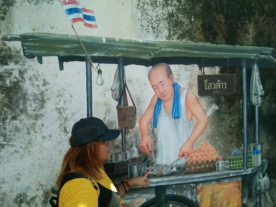 A woman posing with street art depicting a street food stall on Phangnga Road in Phuket Old Town.