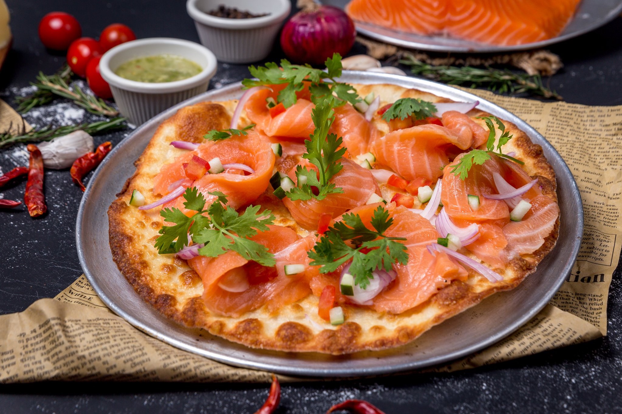 A pizza topped with salmon, coriander, chopped cucumber and chili with a side of seafood sauce straight out the oven at Alice's Pizza. 