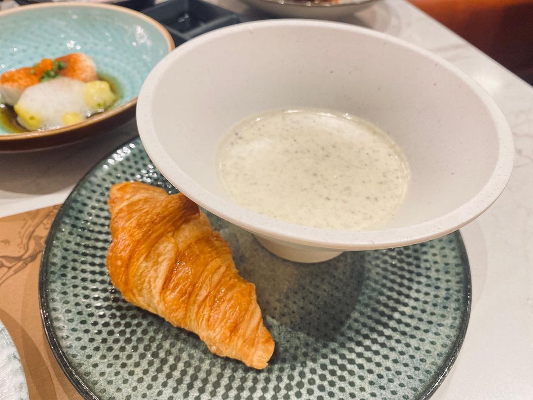 A bowl of fragrant and creamy truffle soup paired with a crunchy croissant. 