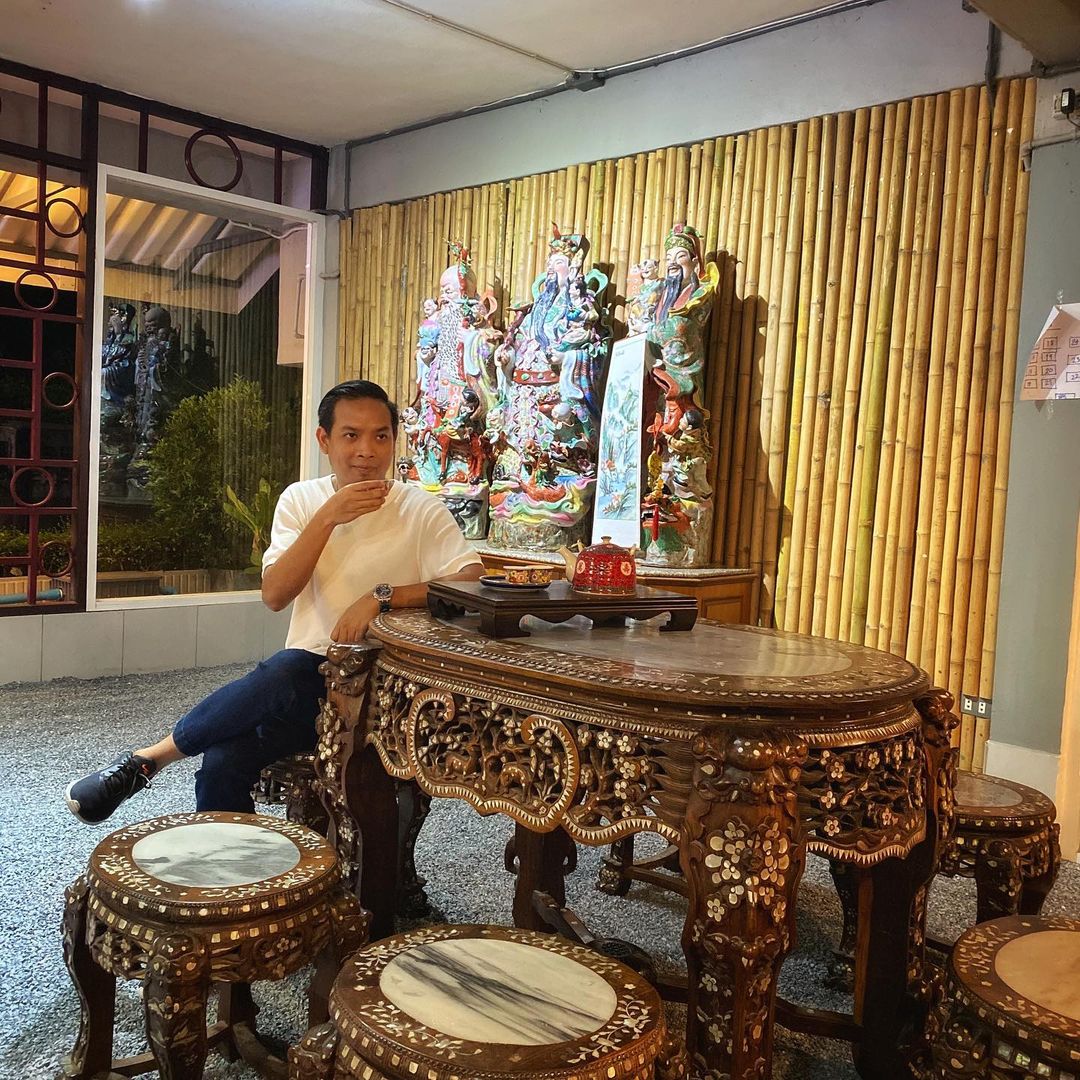 A man seated at an old carved wood table at Khao Tom Gui