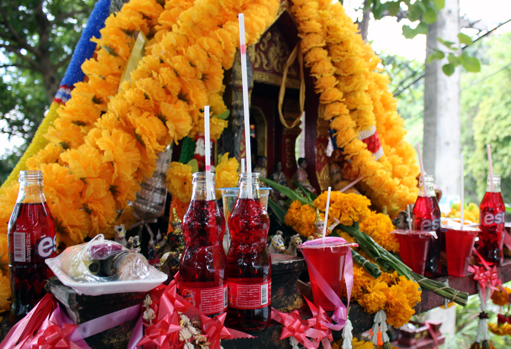 A spirit house with offerings of flowers and red fanta